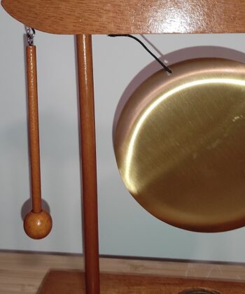 Gong de table avec une structure de bois rouge, disque doré et heurtoir dans un élégant style orientale. Le disque de métal a un diamètre de 12 cm.